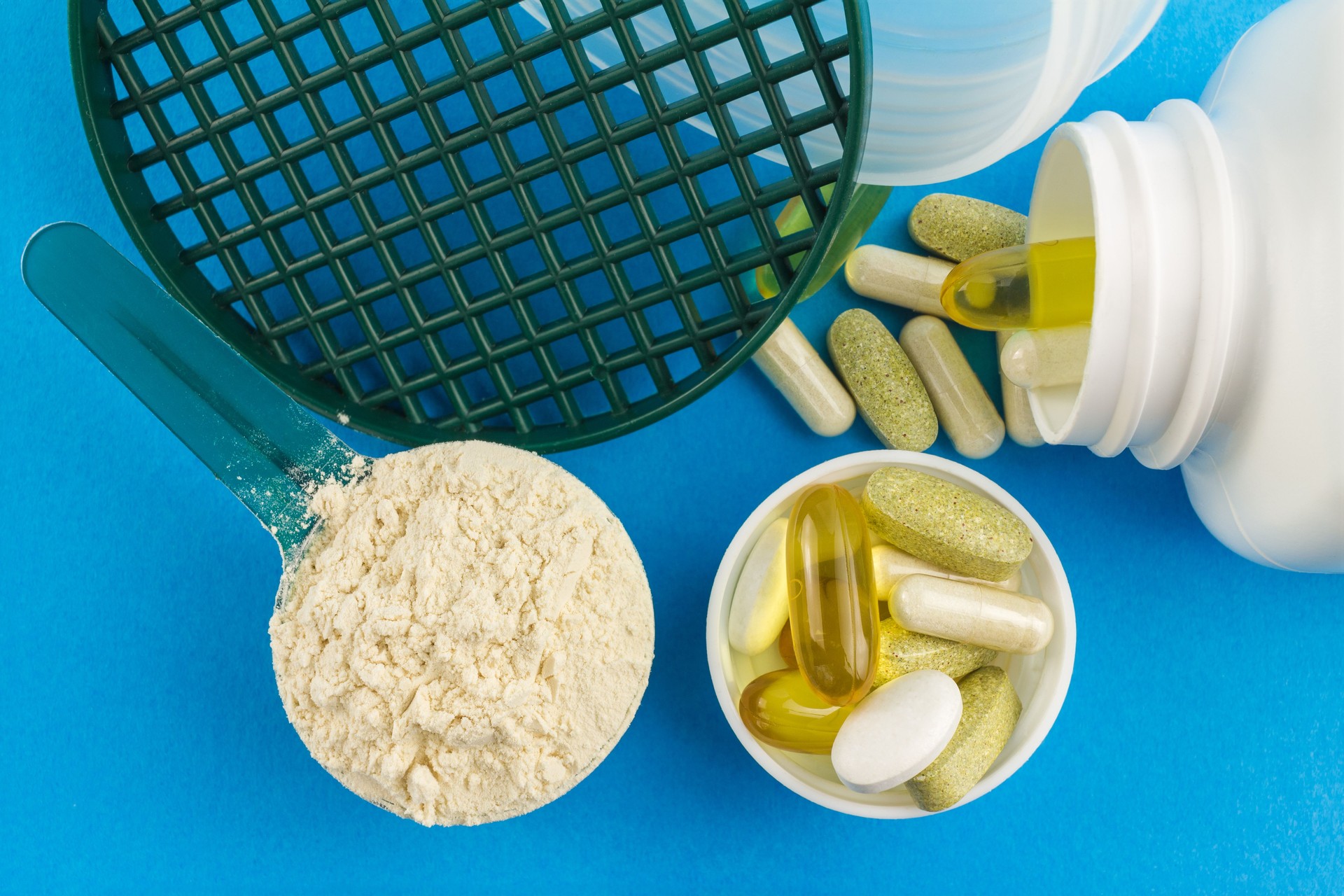Proteína en polvo en la medición de la cuchara de plástico y complejo vitamínico, Omega 3, cápsulas de glucosamina, suplementos sobre fondo azul, nutrición deportiva, vista superior